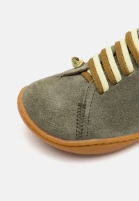 Scarpa in suede verde con lacci gialli e marroni, punta rotonda, suola in gomma e dettagli di cucitura visibili.