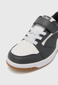 Baskets noires en cuir et blanches en synthétique avec un bout perforé, lacets blancs, bande velcro et semelle en caoutchouc.