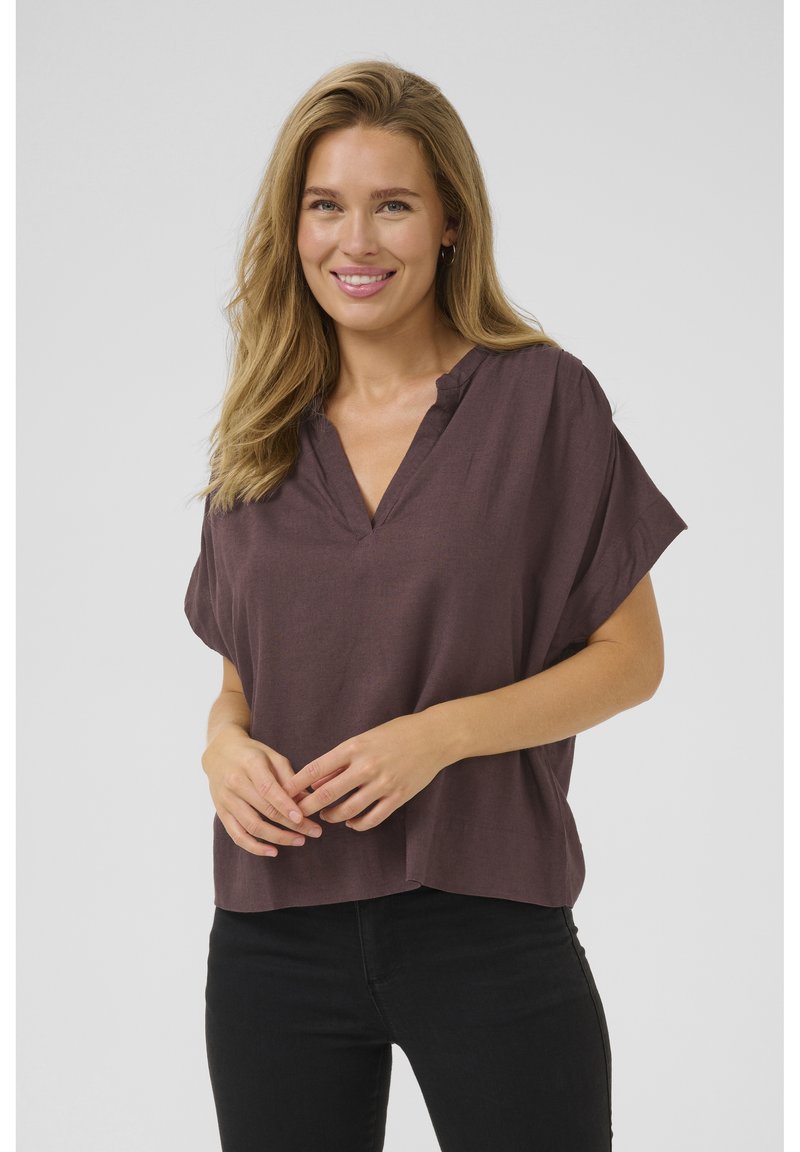 Haut à manches courtes, couleur prune profonde, avec une coupe décontractée et un col en V. Tissu léger avec une légère texture, associé à un pantalon en denim noir.