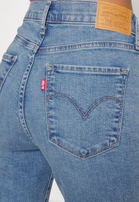 Jeans de mezclilla azules de cintura alta con un acabado texturizado, que presentan un diseño clásico de bolsillo trasero y una etiqueta del logo rojo de Levi's.