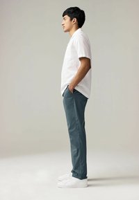 Camicetta bianca a maniche corte, pantaloni teal, scarpe da ginnastica bianche. L'outfit presenta una vestibilità casual con una consistenza uniforme e semplici elementi di design.