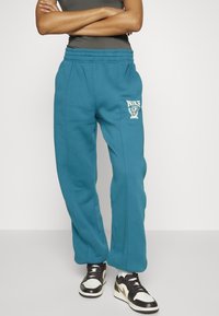 Teal sweatpants tillverkade av mjukt tyg med resår i midjan. Har sidofickor och en grafisk logotyp på vänster ficka. I kombination med sneakers.