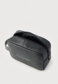 Μαύρη δερμάτινη τσάντα για είδη προσωπικής φροντίδας με φερμουάρ. Διαθέτει διακριτικό λογότυπο και πλαϊνή λαβή για εύκολη μεταφορά. Ομαλή υφή.