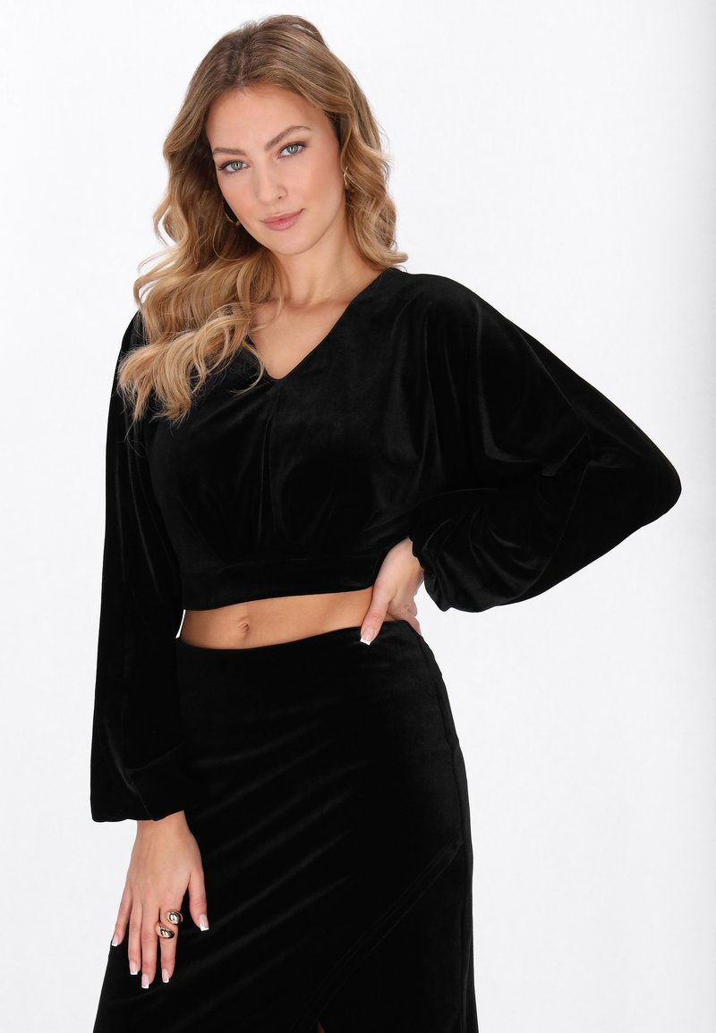 Fekete bársony rövidített felső V-nyakkal, széles ujjakkal és sima textúrával, hozzáillő, testhez simuló szoknyával, oldalsó hasítékkal.