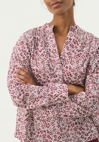 Floral blouse in white and burgundy, featuring a v-neck, long sleeves, gathered details, and a relaxed fit with a lightweight fabric.