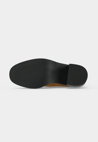 Semelle d'une chaussure habillée vue par en dessous, avec un avant et un talon noir lisse, présentant des zones de préhension texturées au niveau des orteils et du talon.