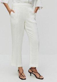 Witte linnen broek met rechte benen, hoge taille en zijzakken, aangevuld met zwarte hakken met bandjes. Gladde textuur met minimale details.