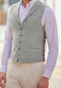 Szara kamizelka w jodełkę z wyciętym kołnierzem, zapinana na guziki z przodu, z kieszeniami, noszona na koszuli w kratę w kolorach czerwonym i niebieskim.