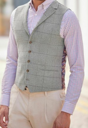 Szara kamizelka w jodełkę z wyciętym kołnierzem, zapinana na guziki z przodu, z kieszeniami, noszona na koszuli w kratę w kolorach czerwonym i niebieskim.