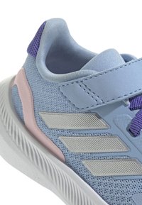 Baskets de sport bleu clair avec une tige texturée, accents violets, panneau latéral rose et rayures argentées. Elles disposent d'une sangle Velcro et d'un col rembourré.