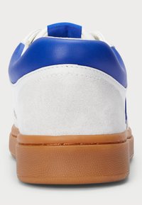 Vit sneakers med en blå läderhälen, grå mockadetalj och en strukturerad gummisula. Släta ytor och rundad form.