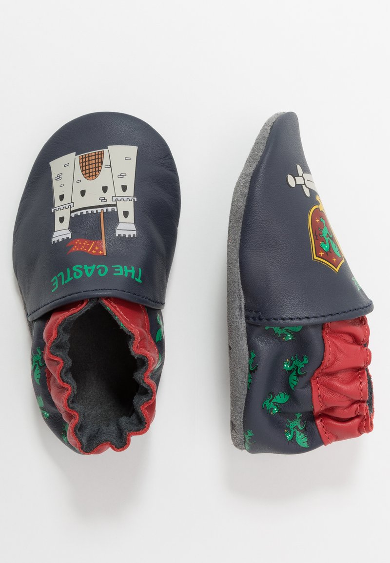 Chaussons en cuir marine pour bébé avec des graphismes de château et de dragon, accents rouges, chevilles élastiques et semelles en feutre gris pour une meilleure adhérence.