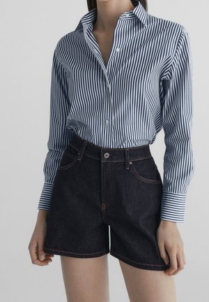 Striped button-down shirt in blue and white, paired with dark denim shorts featuring contrast stitching and pockets.