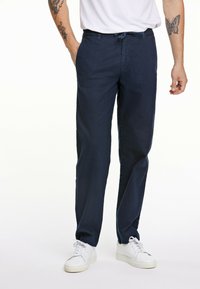 Pantalones casuales azul marino hechos de una tela ligera, con una cintura elástica ajustable y bolsillos laterales, combinados con zapatillas blancas.