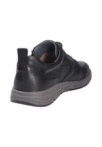 Sneaker nera in pelle con finitura texturizzata, dotata di suola in gomma grigia e linguetta sul retro. Il design include dettagli di cucitura decorativa.