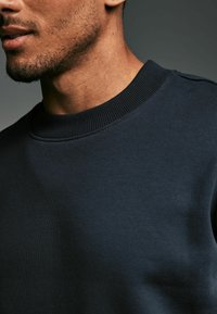 Mörkblå crewneck sweatshirt tillverkad av mjukt bomullstyg, med ribbat halslinne och axlar samt en slät textur.
