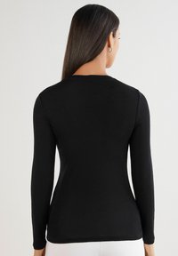 Schwarzes Langarmoberteil aus glattem Stoff, mit Rundhalsausschnitt, tailliertem Schnitt und minimalistischem Design ohne sichtbare Muster oder Verzierungen.
