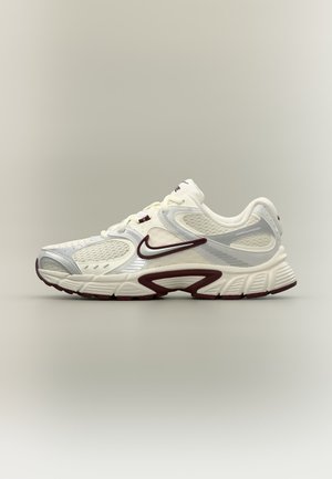 Zapatilla de correr Nike blanca y beige con detalles burdeos y tejido de malla, mostrada de perfil sobre un fondo neutro.