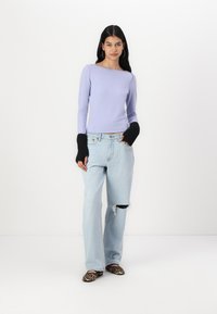 Lilac long-sleeve top with a boat neckline, black ribbed cuffs, paired with light blue high-waisted jeans featuring a ripped knee, and leopard print flats.