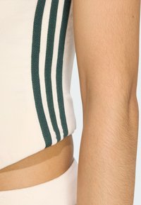 Krémový cropped top s pruhovanými pletenými akcentmi na rukávoch v zelenej a bielej farbe, s hladkou textúrou. Viditeľný detail odkrytého brucha.