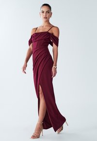 Burgundia värvi õlgadeta kleit, millel on drapeeritud kangas, figuurikohane vöökoht ja reie kõrgune lõhik. Kandmisega kuldsed rihmikud kõrged kontsad ja käevõru.