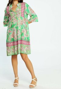 Vestido floral verde con diseño en capas, escote en V y mangas 3/4, acentuado con patrones de borde rosa y confeccionado en tejido ligero.
