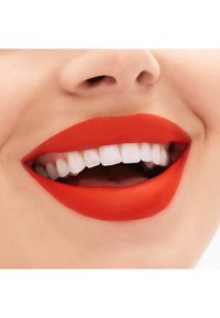 Un rouge à lèvres rouge vif appliqué sur des lèvres lisses, mettant en avant un large sourire avec des dents blanches. Une texture de peau subtile visible autour de la zone de la bouche.