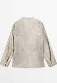 Chemise à manches longues beige clair, en tissu texturé, avec un empiècement dans le dos et des poignets à boutons. Finition lisse, coupe décontractée.