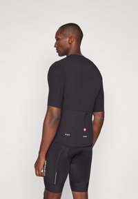 Maillot de cyclisme noir à manches courtes, en tissu texturé, avec une poche à l'arrière. Les accents incluent des dots réfléchissants et un logo près du bas.