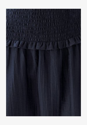 Donkerblauwe jurk met een gerimpelde lichaam, ruffles langs de zoom en een gestructureerd geplooid rokgedeelte.