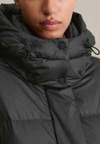 Μαύρο μπουφάν puffer με ψηλό λαιμό. Διαθέτει κουμπιά με τσίγκι και κορδόνια. Λείο, γυαλιστερό υλικό με σχέδιο καπιτονέ.