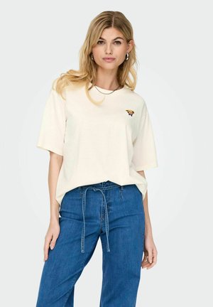 T-shirt en coton oversize crème avec un col rond et des manches courtes, arborant un petit design de chien brodé sur la poitrine gauche.