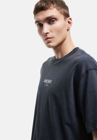 Overdimensioneret sort t-shirt lavet af bomuld. Har rund halsudskæring og broderet tekst på brystet. Blød tekstur og afslappet pasform.