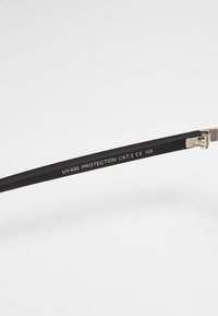Ochelari de soare negri cu un finisaj mat, având balamale metalice și un text care citește "PROTECȚIE UV400 CAT.3 CE 106" pe braț.