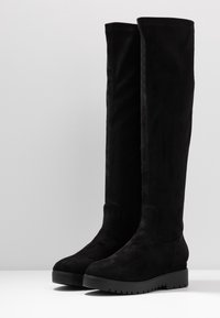 Bottes en daim noir au-dessus du genou avec une semelle plate, présentant un design minimaliste et une texture lisse. Détail de fermeture éclair latérale inclus.