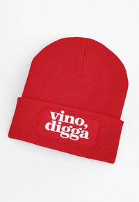 Red knit beanie with a ribbed texture, featuring a rectangular patch in white that displays the text "vino, diggä."