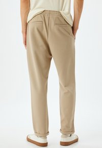 Beige sweatpants med en afslappet pasform, elastisk talje og sidelommer. De har opkrøllede manchetter og en blød tekstur.