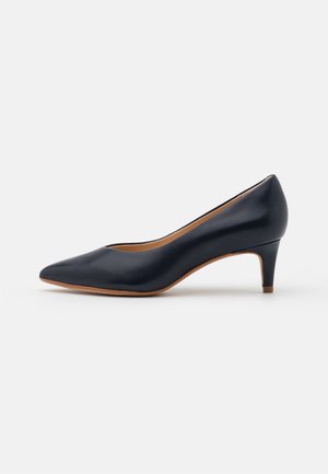 Zapato de salón de piel azul marino con punta afilada, tacón medio delgado y textura suave. Presenta una suela de color marrón claro y un diseño minimalista.