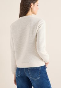 Světlý šedý pruhovaný mikina s dlouhými rukávy a kulatým výstřihem. Měkká textura, volný střih, kombinovaná s modrými džínami. Jednoduchý design.