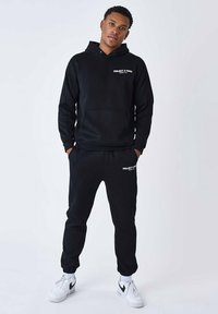 Conjunto de sudadera con capucha y pantalones jogger de mezcla de algodón. La sudadera tiene un bolsillo frontal y un logo. Las zapatillas tienen un diseño clásico en blanco y negro.