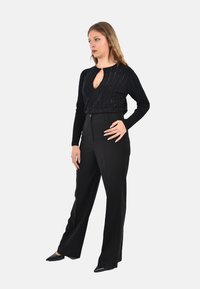 Top lungo aderente a coste nero con scollatura ovale, abbinato a pantaloni neri a vita alta e scarpe nere a punta. Texture del tessuto liscia.