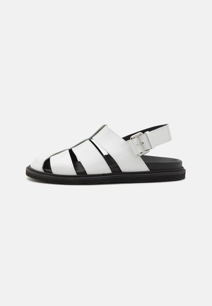White leather sandal with multiple cutouts, adjustable ankle strap, and black sole. Smooth texture and minimalistic design.
