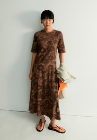 Brown tie-dye maxi dress with short sleeves, soft fabric, and a relaxed fit. Features a label on the hem and contrasting sandals.