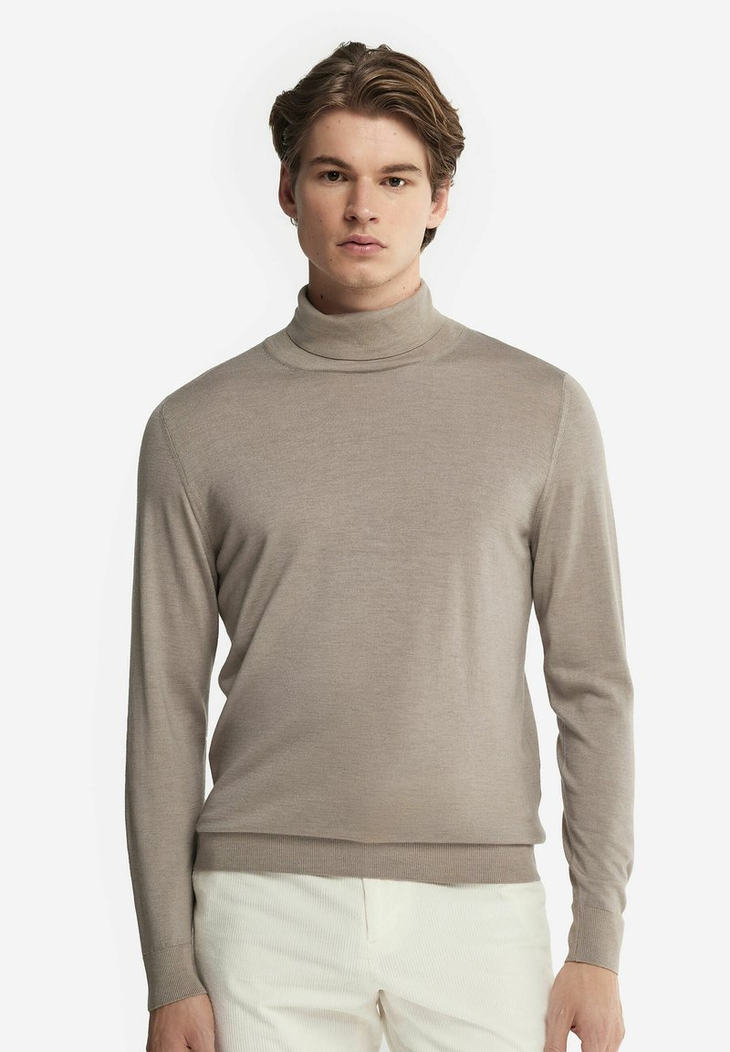 Ljust beige polotröja gjord av ett mjukt material. Har långa ärmar och en kroppsnära design, med ribbad halsringning och fåll.