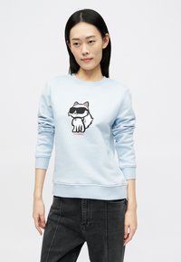 Sweatshirt azul claro feito de material suave, com um design de um cão de desenho animado usando óculos de sol e detalhes em preto e vermelho.