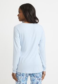 Ljusblå långärmad topp med avslappnad passform, rund halsringning och mjukt tyg. I kombination med mönstrade blå och vita byxor med blommotiv.