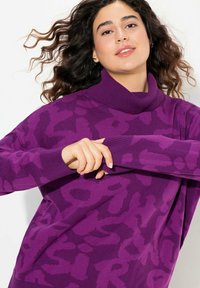 Pull violet avec un col montant, présentant un motif texturé. Tissu tricoté avec des manches longues et des poignets côtelés. Apparence douce et confortable.