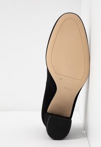Semelle de chaussure noire avec dessous beige, taille 42,5, marque « högl » visible près du talon, reposant en angle contre une surface blanche.