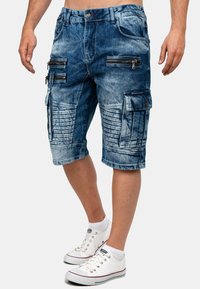 Pantaloni cargo in denim blu sbiadito con diverse tasche con zip e dettagli testurizzati. Presentano una vestibilità regolare e un design lunghezza ginocchio.