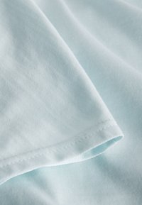 Hellblauer Stoff mit glatter Textur, zeigt eine gefaltete Kante und Nähte, die seine weiche und gleichmäßige Oberfläche hervorheben.